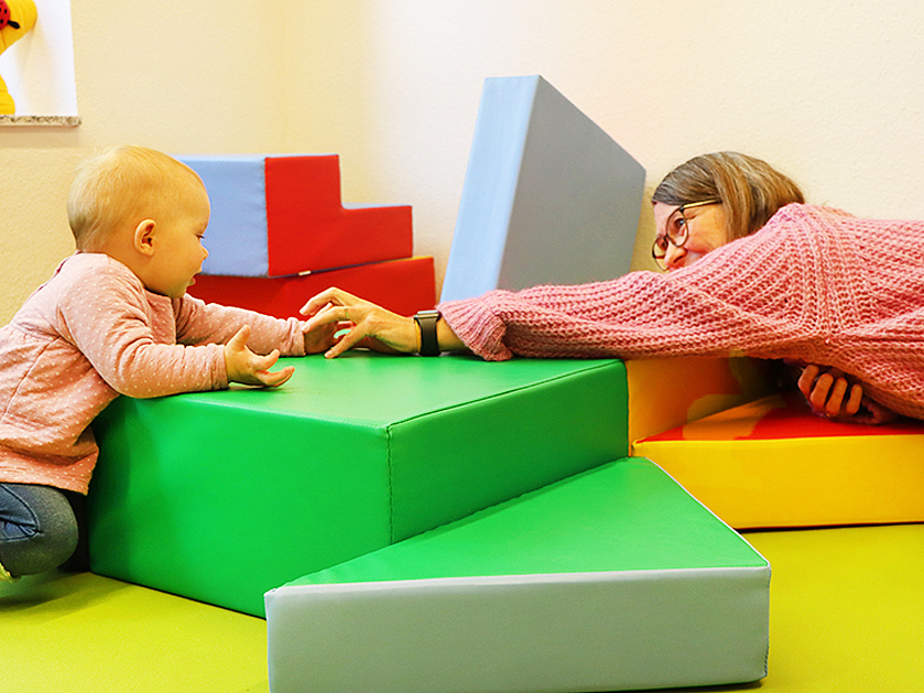 kleines Mädchen und Betreuerin spielen auf großen Softbausteinen