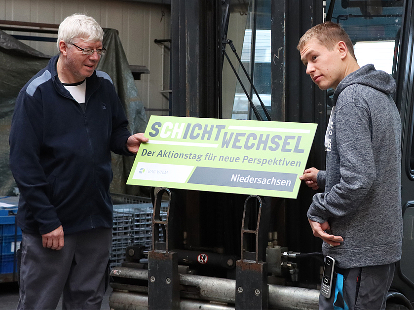 zwei Arbeiter halten ein SCHICHTWECHSEL-Schild