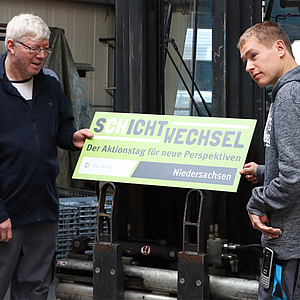 zwei Arbeiter halten ein SCHICHTWECHSEL-Schild