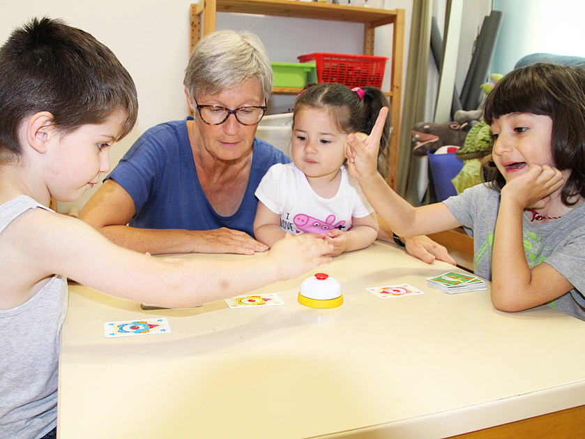 drei Kinder spielen ein Kartenspiel mit ihrer Frühförderin