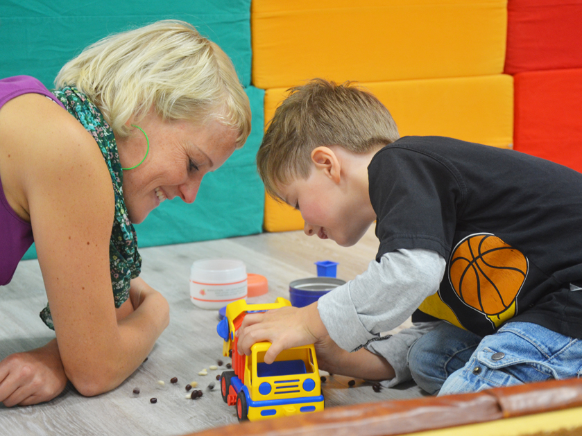 kleiner Junge und seine Frühförderin spielen mit einem Spielzeugauto
