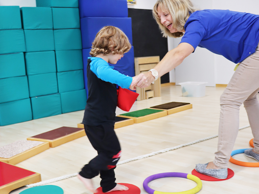 kleiner Junge mit seiner Frühförderin bei einer Motorikübung