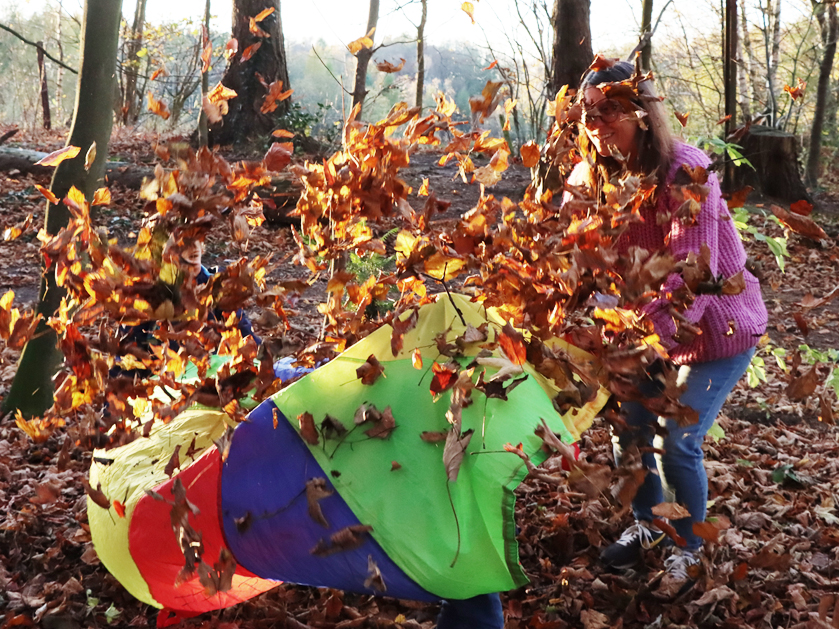 Frühförderin und Kind wirbeln Herbstblätter auf