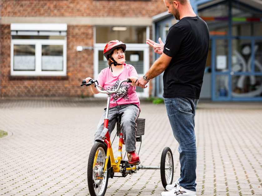 Betreuer der Gerd-Hahlbrock-Werkstatt bringt Frau Fahrradfahren bei