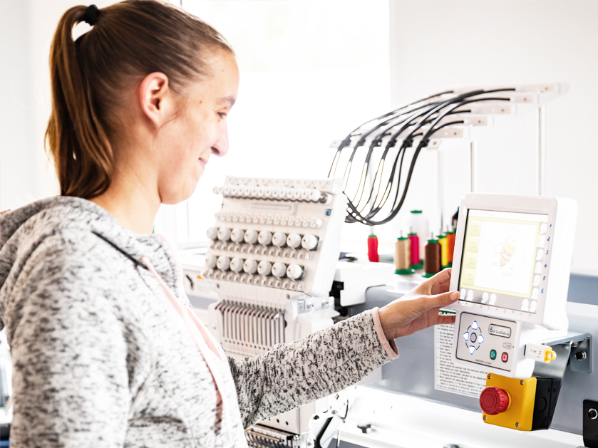 Mitarbeiterin stellt beim Einstellen einer Bestickung an der Maschine