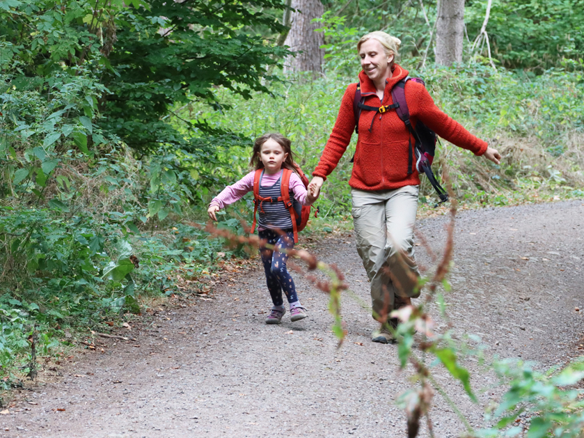 Erzieherin und kleines Mädchen rennen dem Waldweg entlang
