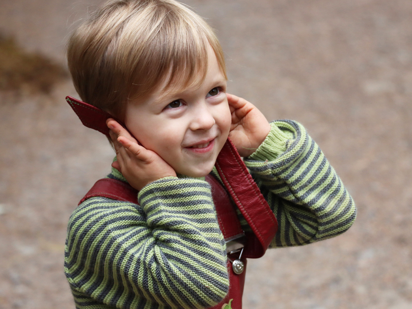 kleiner Junge lächelt und hält sich die Ohren zu