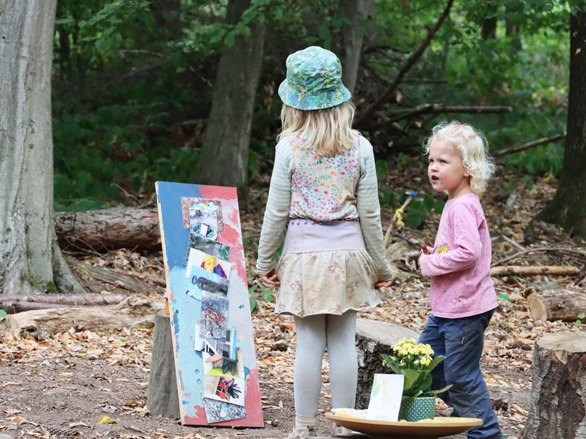 zwei kleine Mädchen vom Waldkindergarten "Waldtentdecker" betrachten ein buntes Brett voll von Fotos