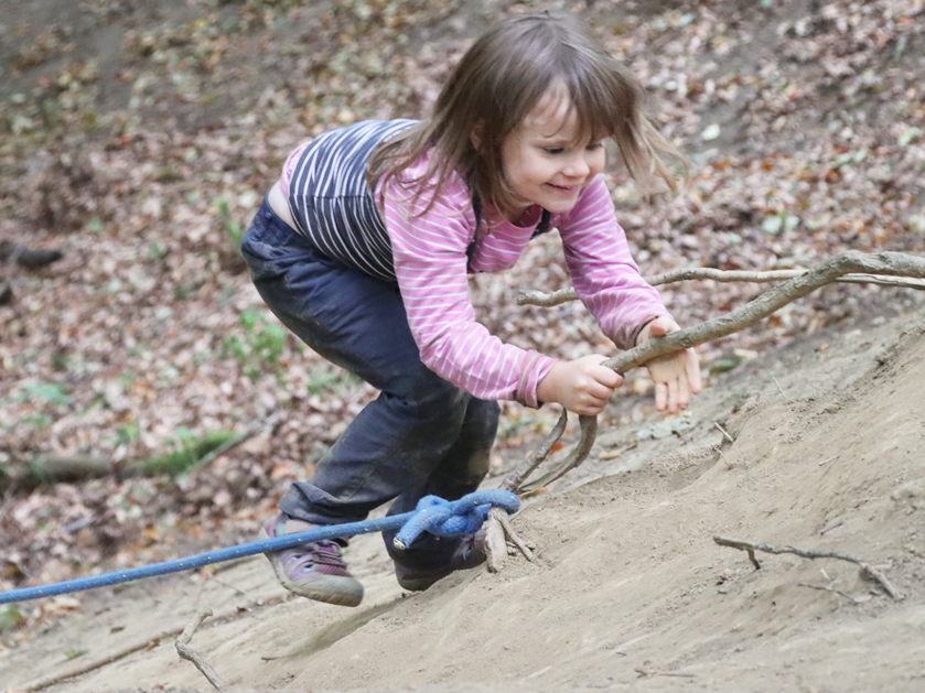 kleines Mädchen klettert die Waldrutsche an einem Seil hoch